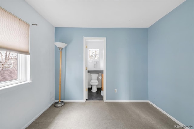 unfurnished bedroom with carpet floors, multiple windows, baseboards, and ensuite bath