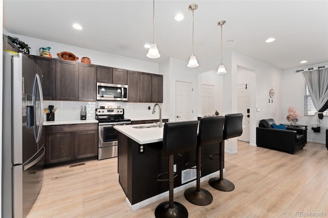 kitchen featuring sink, decorative light fixtures, stainless steel appliances, a breakfast bar area, and dark brown cabinetry