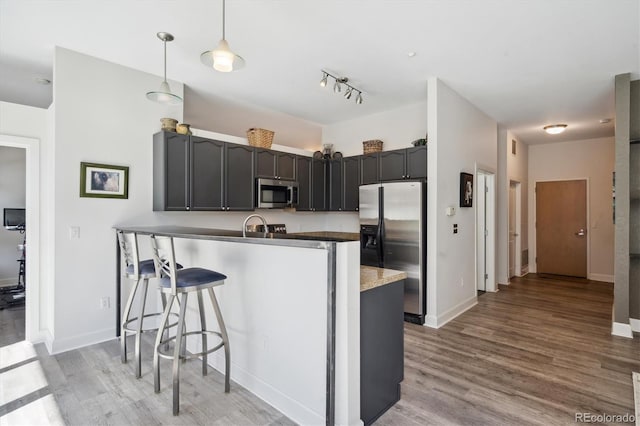 kitchen featuring stainless steel appliances, a peninsula, a kitchen breakfast bar, light wood finished floors, and decorative light fixtures