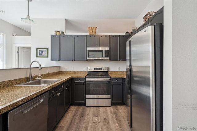 kitchen with stainless steel appliances, a sink, wood finished floors, and decorative light fixtures