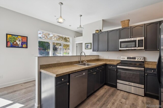 kitchen with stainless steel appliances, a sink, wood finished floors, and dark countertops