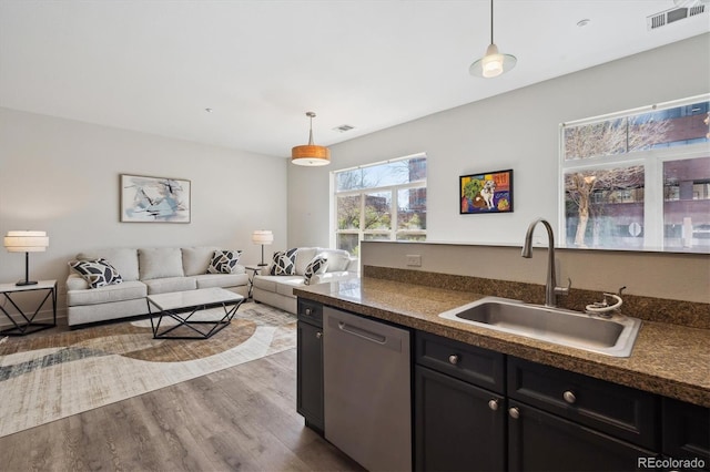 kitchen featuring a sink, stainless steel dishwasher, dark countertops, and dark wood finished floors