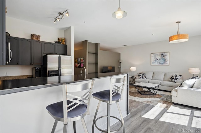 kitchen with stainless steel fridge, dark countertops, open floor plan, a kitchen breakfast bar, and light wood finished floors