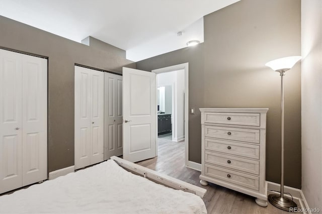 bedroom featuring multiple closets, wood finished floors, and baseboards