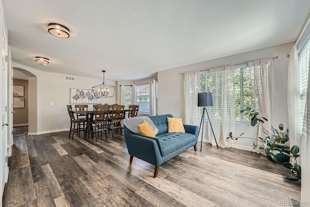 living area featuring baseboards, visible vents, arched walkways, dark wood-type flooring, and a textured ceiling