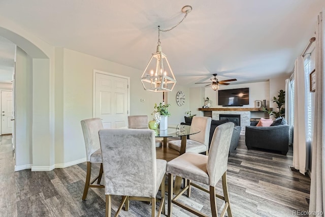 dining room featuring a glass covered fireplace, dark wood-style floors, arched walkways, and baseboards