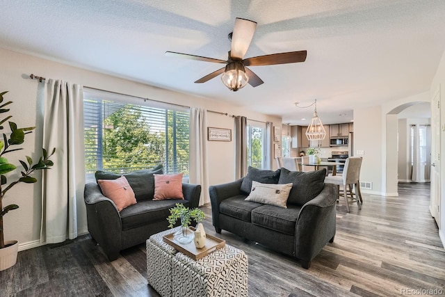 living area featuring visible vents, baseboards, arched walkways, a ceiling fan, and dark wood-style flooring