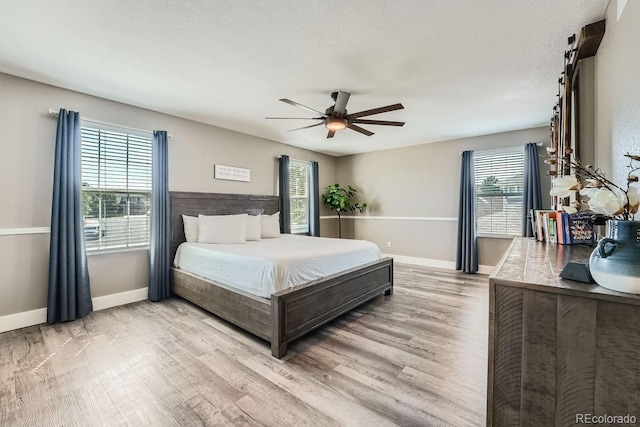 bedroom with baseboards, multiple windows, a textured ceiling, and light wood finished floors