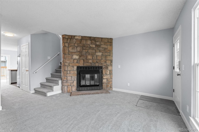 unfurnished living room featuring a stone fireplace, carpet floors, and a textured ceiling