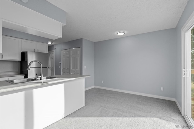 kitchen with light carpet, stainless steel fridge, a textured ceiling, sink, and white cabinetry