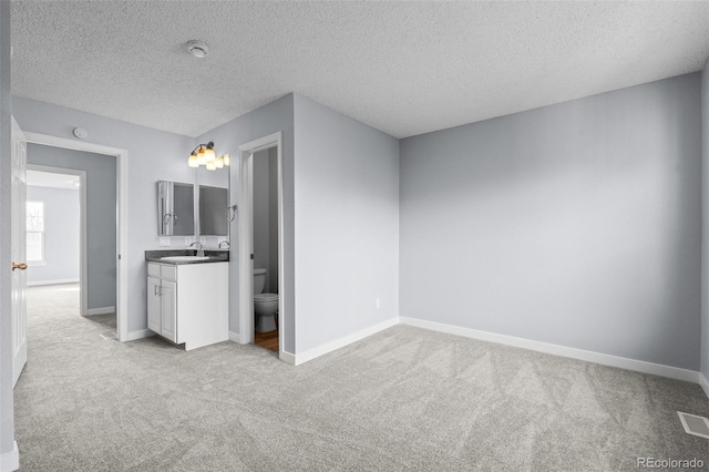 unfurnished bedroom with light carpet, a textured ceiling, ensuite bathroom, and sink