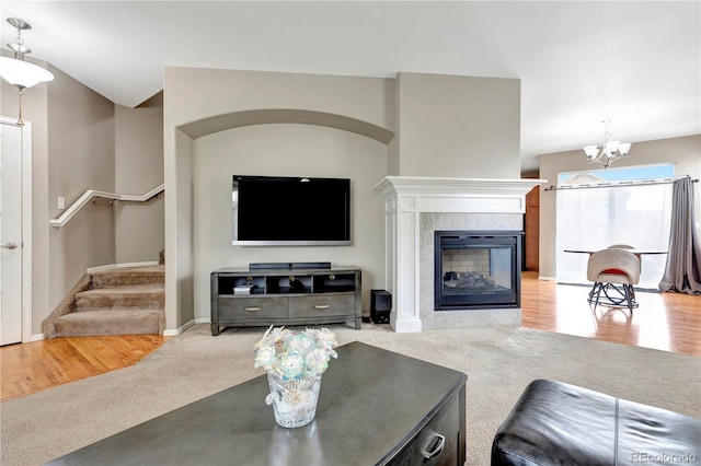 carpeted living area featuring a chandelier, a tile fireplace, stairway, and wood finished floors