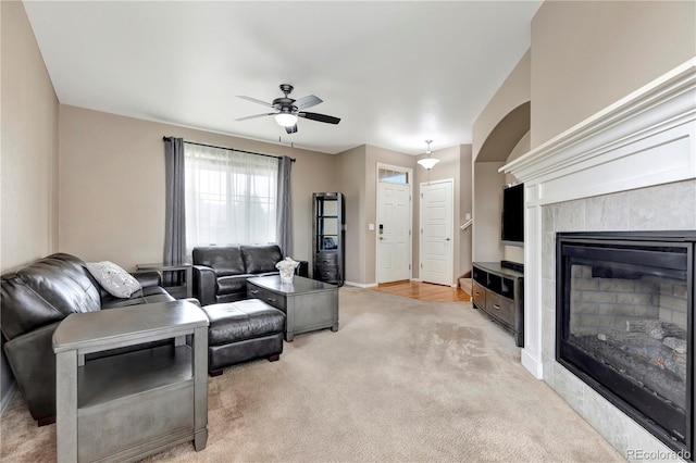 living room featuring a ceiling fan, a glass covered fireplace, light carpet, and baseboards