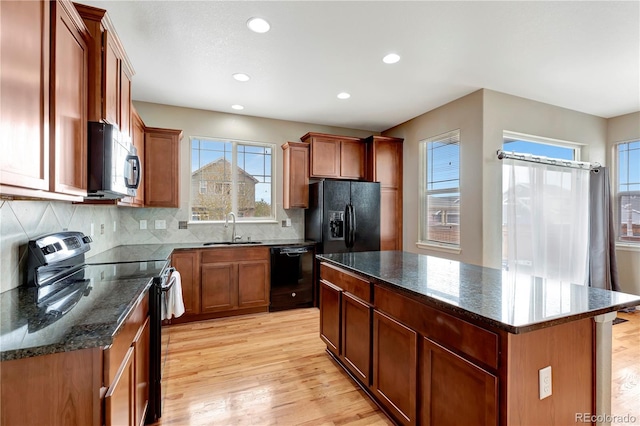 kitchen with black appliances, light wood-style flooring, a kitchen island, and a sink