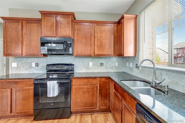 kitchen with dark stone counters, a sink, light wood finished floors, and black appliances