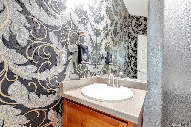 bathroom with wallpapered walls, a textured wall, and vanity