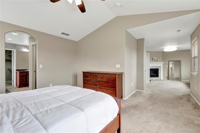 bedroom featuring arched walkways, lofted ceiling, light carpet, a fireplace, and visible vents