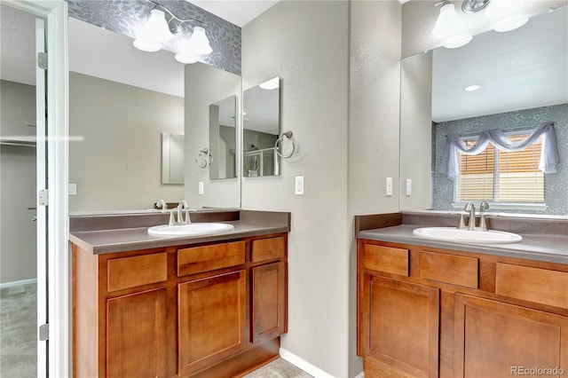 full bath featuring baseboards, two vanities, and a sink