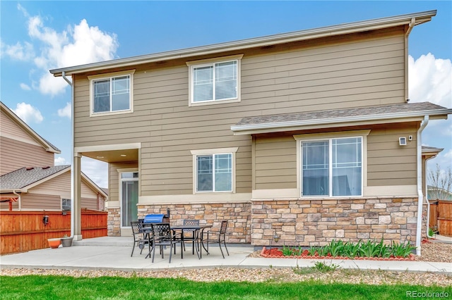 back of house featuring stone siding, a patio, and fence