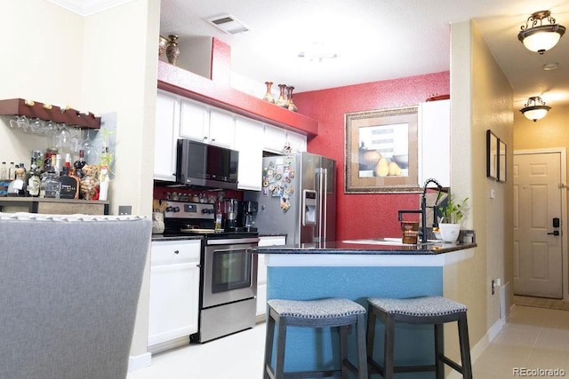 kitchen featuring appliances with stainless steel finishes, a kitchen bar, kitchen peninsula, and white cabinets