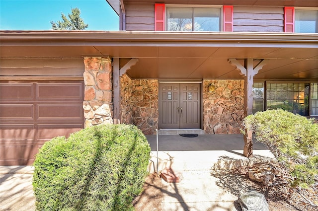 doorway to property with covered porch, stone siding, and a garage