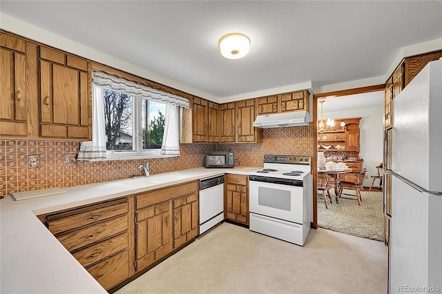 kitchen with white appliances, under cabinet range hood, a sink, and brown cabinets
