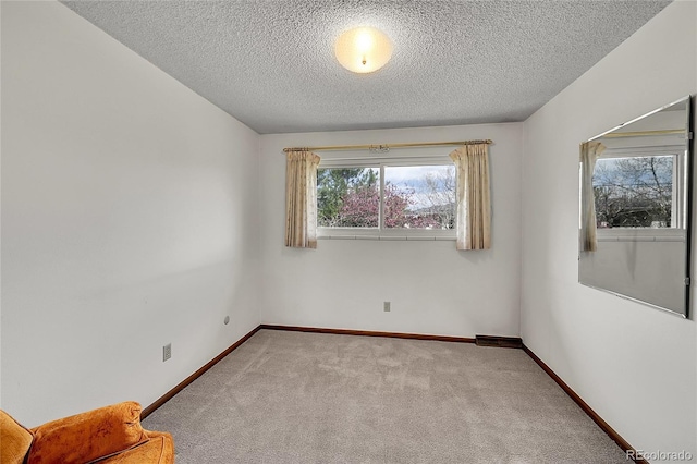 carpeted spare room featuring a textured ceiling and baseboards