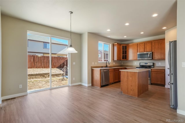 kitchen with sink, decorative light fixtures, a center island, light hardwood / wood-style flooring, and stainless steel appliances