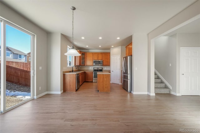 kitchen with sink, a center island, hanging light fixtures, stainless steel appliances, and light hardwood / wood-style floors