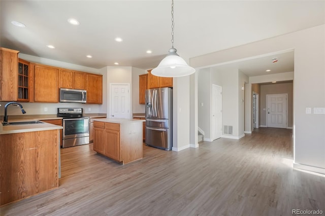 kitchen with pendant lighting, sink, light hardwood / wood-style flooring, appliances with stainless steel finishes, and a center island