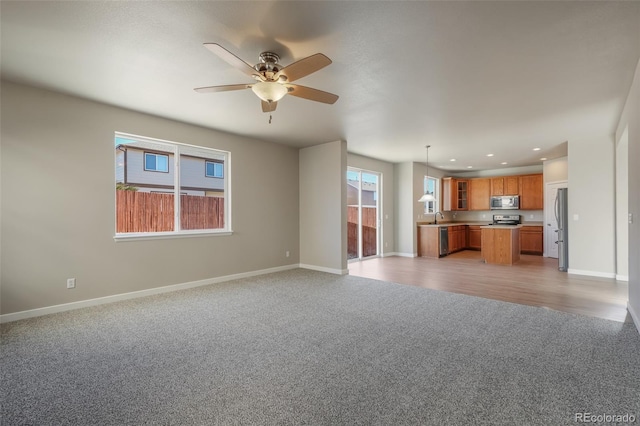 unfurnished living room with ceiling fan, sink, and light carpet