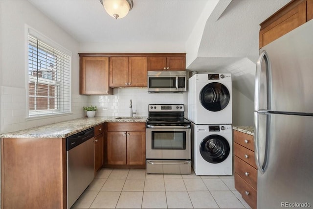 2872 Jasmine St, Denver, CO 80207 - kitchen featuring appliances with stainless steel finishes, stacked washer / dryer, a sink, brown cabinetry, and decorative backsplash