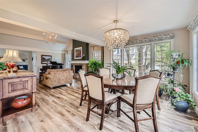 dining area featuring a chandelier, a stone fireplace, and light hardwood / wood-style flooring