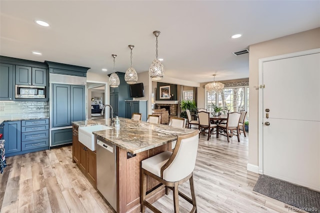 kitchen featuring built in appliances, light wood-type flooring, sink, and a large island with sink