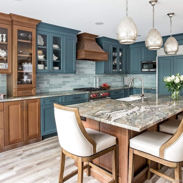 kitchen featuring tasteful backsplash, light stone counters, decorative light fixtures, custom range hood, and appliances with stainless steel finishes