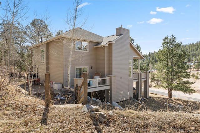 back of property with a shingled roof and a chimney