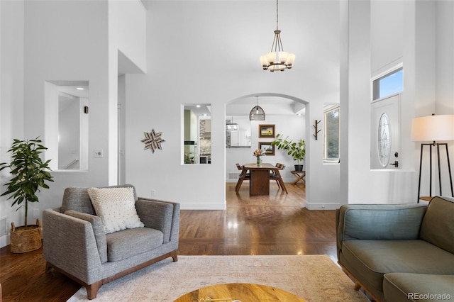 living room featuring arched walkways, baseboards, a towering ceiling, and wood finished floors