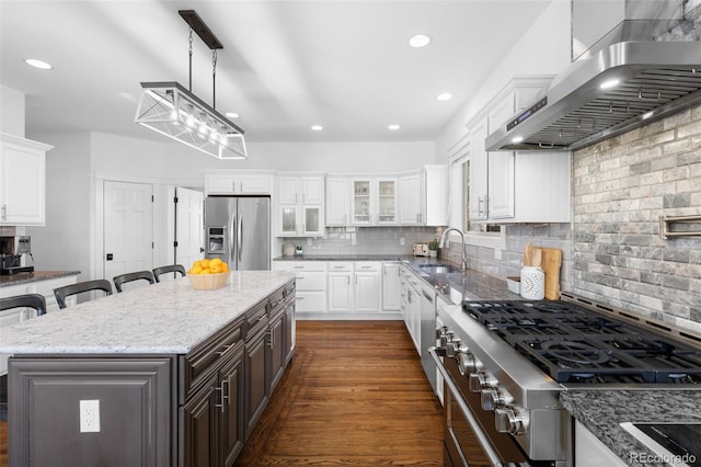 kitchen with a sink, stainless steel appliances, white cabinets, wall chimney exhaust hood, and backsplash