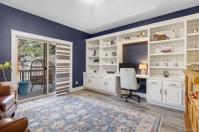 home office with light wood finished floors, built in study area, and baseboards