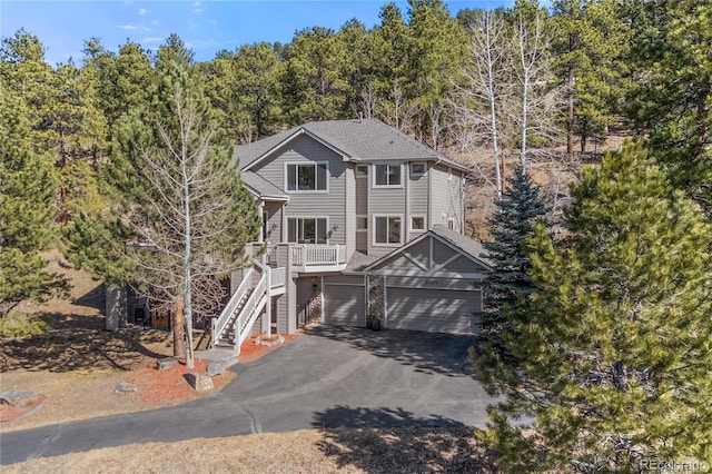 view of front of property featuring stairway, an attached garage, driveway, and roof with shingles