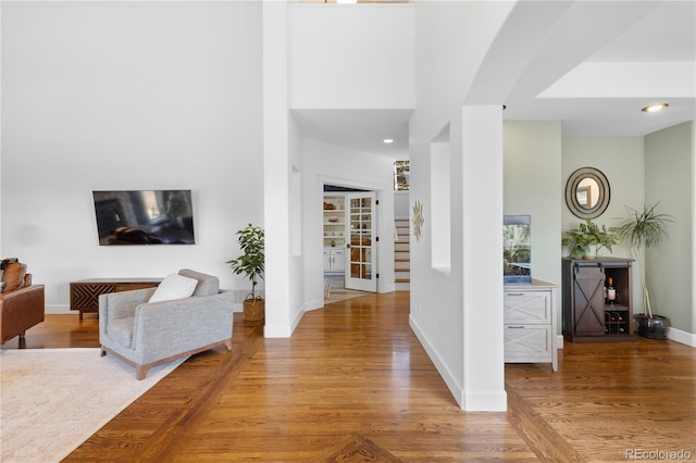 hallway with recessed lighting, a high ceiling, baseboards, and wood finished floors