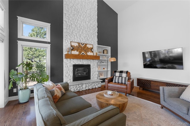 living area featuring a stone fireplace, high vaulted ceiling, baseboards, and wood finished floors