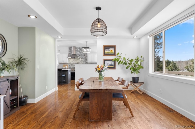 dining space with recessed lighting, baseboards, a raised ceiling, and wood finished floors