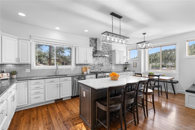 kitchen featuring a sink, dark wood-type flooring, dishwasher, and wall chimney range hood