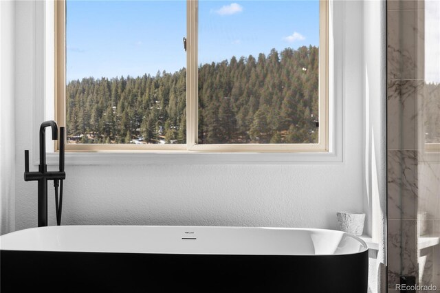 full bath with a textured wall, a wooded view, and a freestanding bath