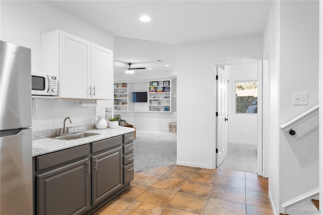 kitchen featuring white microwave, freestanding refrigerator, gray cabinetry, a sink, and light colored carpet