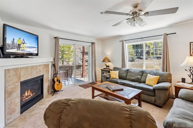 living room featuring a ceiling fan, a tile fireplace, and light colored carpet