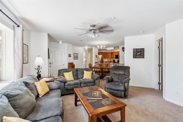living room featuring light carpet, baseboards, and ceiling fan with notable chandelier