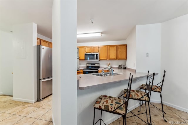 kitchen with a peninsula, light tile patterned floors, a kitchen bar, a sink, and appliances with stainless steel finishes