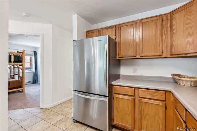 kitchen with freestanding refrigerator, light tile patterned flooring, brown cabinets, light countertops, and light colored carpet